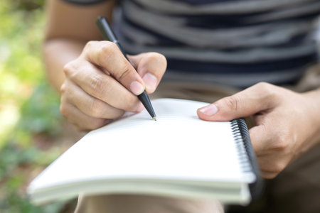 close up hand young man are sitting using pen writing Record Lecture notepad into the book in the park.の写真素材