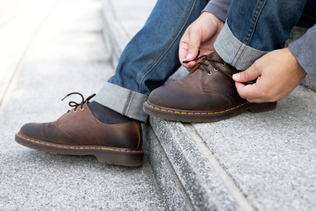 people man in jeans tie up shoelace on wearing brown leather shoes sitting staircase background....