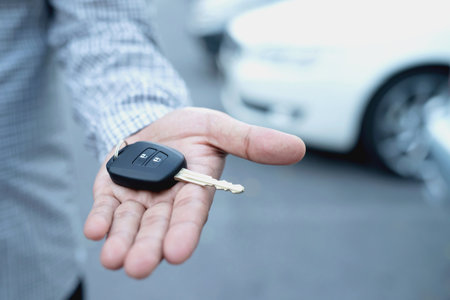 Car key, businessman handing over gives the car key to the other man on car background.