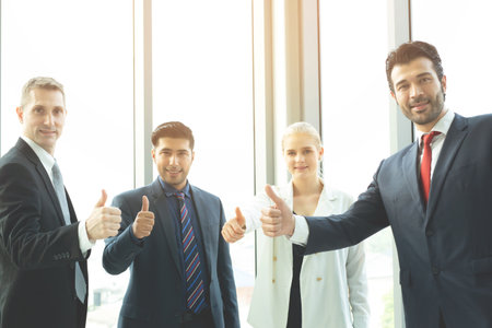 Happy Multiracial Group Of Business People Raising Arms Over office Background Successful entrepreneurs. Thumbs up Success Business team achieving goals.の写真素材