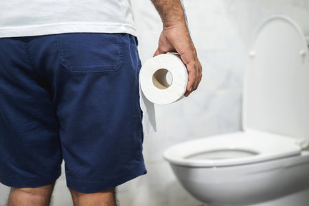man suffers from diarrhea holds toilet paper roll in front of toilet bowl. Stomach
