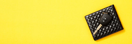 Wallet with new car keys on yellow background.