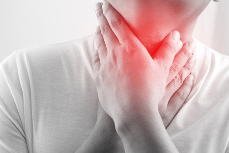 sore throat pain. Closeup of young man sick holding her inflamed throat using hands to touch the ill neck in blue shirt on gray background. Medical and healthcare concept. Focus red on to show pain.の写真素材