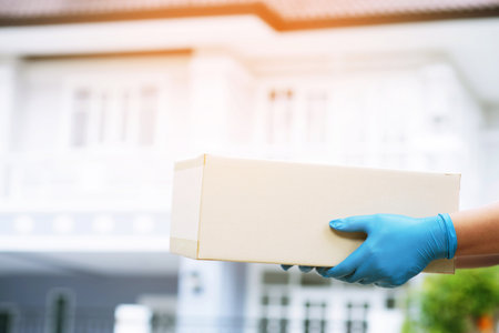 parcel delivery man wear protective gloves blue and mask, protect Hygiene germ and bacteria of a package through a service send to home. hand holding consign and submission customer accepting a of boxの写真素材