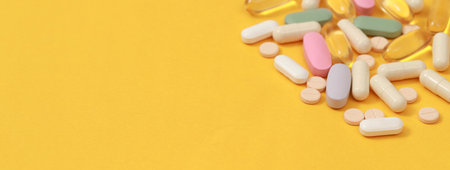 Pill bottle spilling out. colorful pills on to surface tablets on a table yellow background. top...