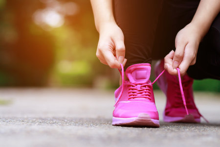 Running shoes pink. close up female athlete tying laces for jogging on road. Runner ties getting ready for training. Sport lifestyle.の写真素材