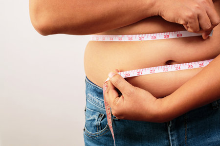 fat man check out body overweight abdomen his belly with in hand measuring tapeの写真素材