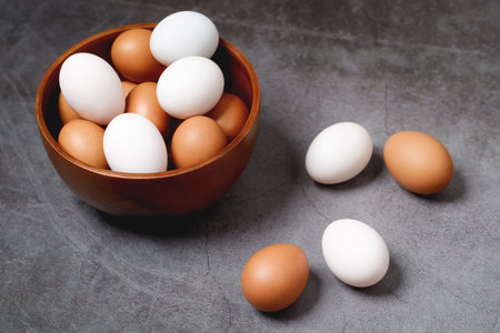 White and brown eggs in a wooden bowl on a gray background.