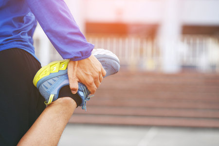 young man runner stretching for warming up before running or working out on the road. Track and Field Athlete exercise. Fitness and sport healthy lifestyle concept. copy space banner.の写真素材