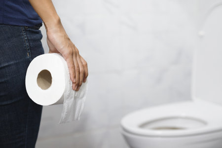 portrait of a woman suffers from diarrhea his stomach painful. ache and problem. hand hold tissue paper roll in front of toilet bowl. constipation in bathroom. Hygiene, health care concept.の写真素材