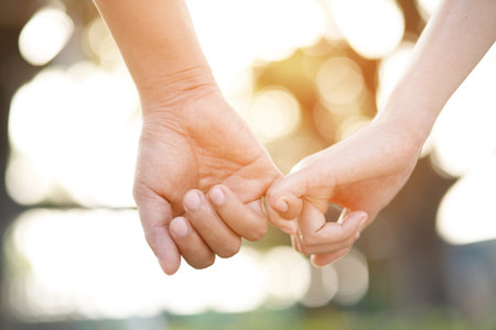 Couple lovers romantic holding hands towards with bright sun flare in public parks, or close up view in a conceptual image first love adolescent young relationship. loverの写真素材