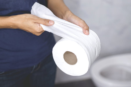 portrait of a woman suffers from diarrhea his stomach painful. ache and problem. hand hold tissue paper roll in front of toilet bowl. constipation in bathroom. Hygiene, health care concept.の写真素材