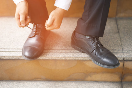 Close up of businessman hand tie shoelaces wearing leather shoes sitting on staircase background.の写真素材