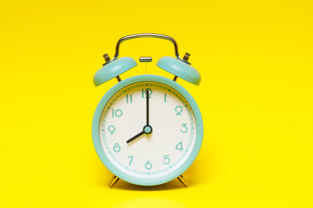 vintage retro alarm clock eight minutes to twelve time o'clock on  yellow background.の写真素材