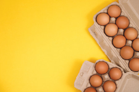 Chicken eggs in a cardboard box ready to cook on a yellow background
