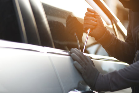 Close up car thief hand holding screwdriver tamper yank and glove black stealing automobile trying door handle to see if vehicle is unlocked trying to break into inside.の写真素材