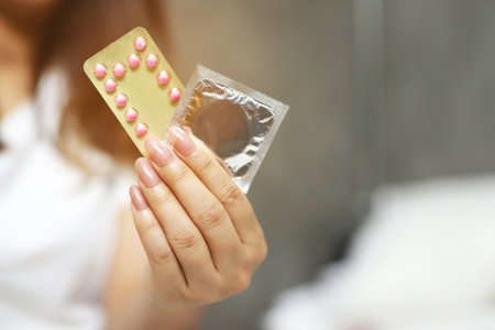 Contraceptive means: Woman hand holding contraceptive pills and condom sitting on sofa background. Protection, safe sex. Contraception, concept birth control. Copy spaceの写真素材