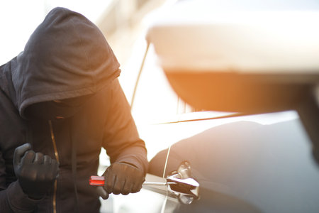 Close up car thief hand holding screwdriver tamper yank and glove black stealing automobile trying door handle to see if vehicle is unlocked trying to break into inside.の写真素材