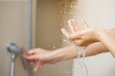 A woman uses hand to measure the water temperature from a water heater before taking a showerの写真素材