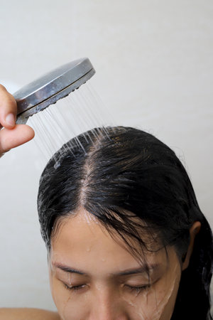 A woman is taking a shower and washing her hair in the bathroom.の写真素材
