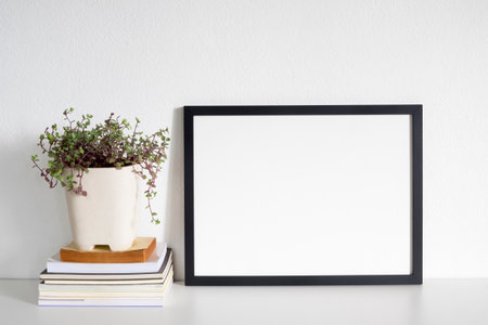 modern blank frame poster with book and plant pot on desk
