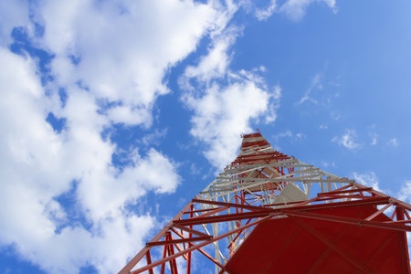 A red white telecommunications tower with blue sky and white clouds.