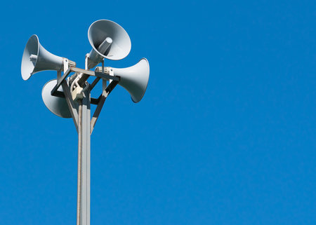 A tall column with four gray loudspeakers in a circle against a clean blue sky. Hazard warning system. The possibility of placing your test or image.の写真素材