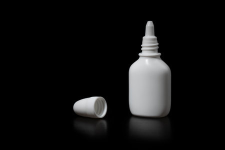 A white liquid bottle with a cap on a black background, a side view close-up.