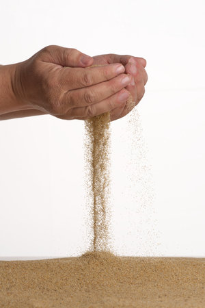 Freeze motion. Men's hands held in a handful of yellow sand which from below falls on a pile.の写真素材