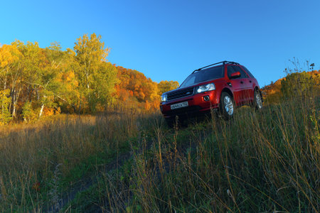 RUSSIA, Rep. of BASHKORTOSTAN, Kugarchinsky District, MRAKOVO village - SEPTEMBER 27, 2020. LAND ROVER FREELANDER 2 red SUV descending dirt road, autumn forest, travel car.のeditorial素材