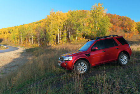 RUSSIA, Rep. of BASHKORTOSTAN, Kugarchinsky District, MRAKOVO village - SEPTEMBER 27, 2020. A red LAND ROVER FREELANDER 2 SUV stands on a dirt road, in the background an autumn forest growing on a hillside.のeditorial素材