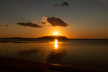 Beautiful fiery red sunrise over the top of the mountainous island of Tiran. Sandy shore of the Red Sea.の写真素材