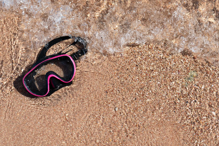 A diving mask lies on a sandy beach and is washed by waves of water. Free space for your materials. A photo with a high resolution.の写真素材