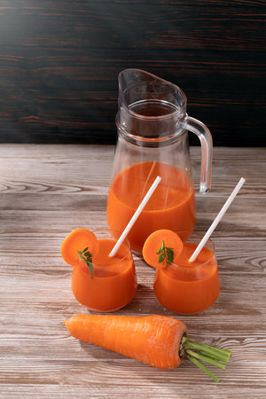On the wooden table there are carrots, a jug and two glasses of fresh juice. Soft light illuminates the objects.の写真素材