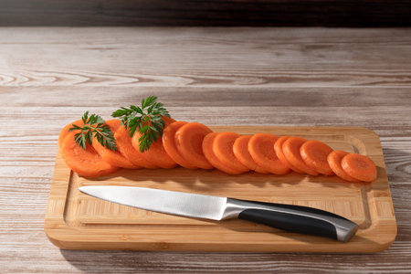 Freshly sliced carrots and a knife lay on a bamboo cutting board. Soft light illuminates the wooden table.の写真素材