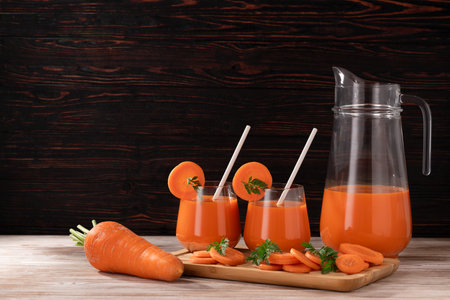 On a wooden table, there are carrots, a jug and two glasses of fresh juice with carrot pieces. Food made from natural products.の写真素材
