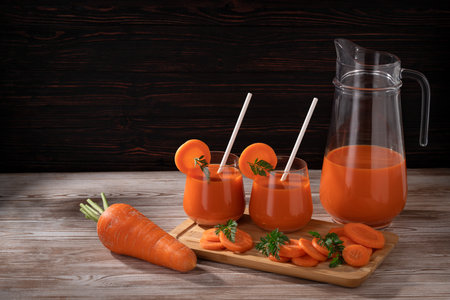 On a wooden table, there are carrots, a jug and two glasses of fresh juice with carrot pieces. Food made from natural products.の写真素材