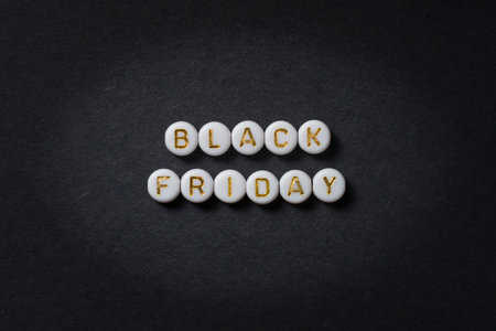 Black Friday text made of round beads in gold letters on black paper, advertising banner with space...