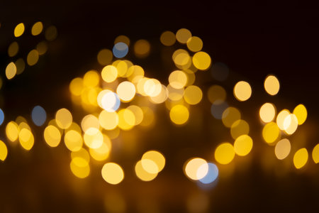 Soft golden bokeh rays create an abstract, festive, glowing pattern against a dark background....