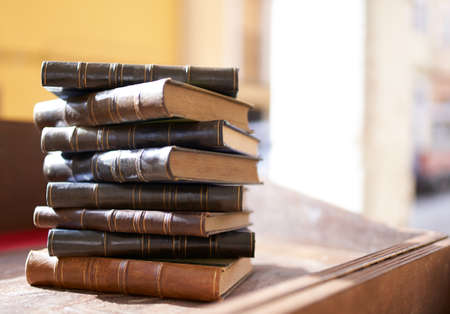 several old and slightly worn books stacked in a tower on a deskの写真素材