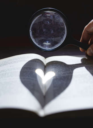 Hand holding a magnifying glass shading a heart on an open book