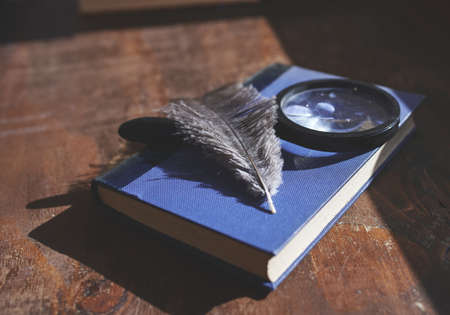 Old blue book with a magnifying glass and feather on top, on a wooden deskの写真素材