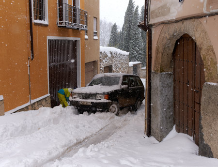 Brihuega, Spain - January 9, 2021: A car stuck in the middle of a street in Brihuega (Spain) while a person tries to put chains on it due to the polar snow storm Filomena.のeditorial素材