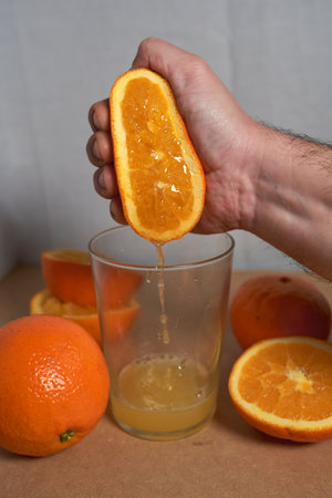 Male hand squeezing an orange into a glass.