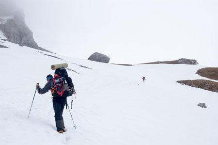 Snow hiker walking on a snowy hillside on a cloudy day in Picos de Europa mountains, Spainの写真素材