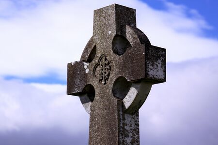 Common celtic cross in an Irish cemetery with blue sky in the backgroundの写真素材