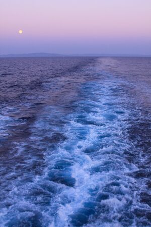 Deep blue, violet sky and boat trail at sunset, with island in the backgroundの写真素材