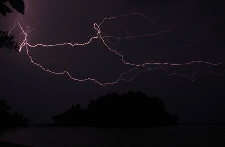 Island silhouette and lightning during night storm. Almost black night picture with electrifying thunderstorm lightsの写真素材
