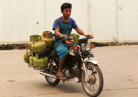 JAKARTA, INDONESIA - May 30, 2013: Indonesian delivery worker on motorcycle stacked with butane gas tanksのeditorial素材