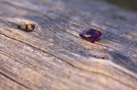 Purple amethyst gemstone on wooden background. The amethyst is violet in color and this stone is cut...